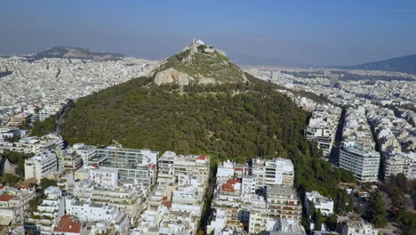 Wide-orbiting-sunny-aerial-of-Mount-Lycabettus-Athens-Greece,-4K