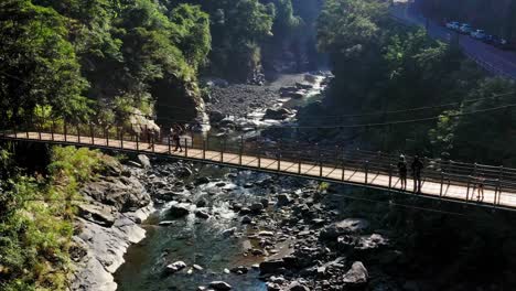 People-crossing-wooden-bridge-in-green-mountains-of-Wulai-district-in-Taiwan-during-sunlight