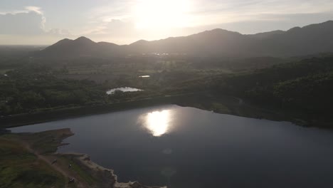 4K-Aerial-Footage-of-Khlong-Bod-Reservoir-with-Sunlight-Over-Mountains-in-Background-in-Nakhon-Nayok,-Thailand