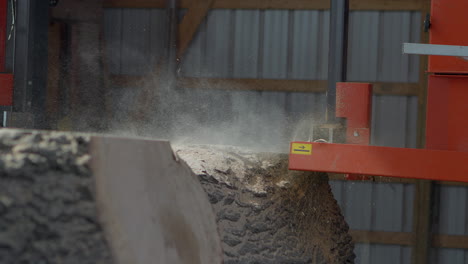 Medium-view-of-a-saw-at-a-sawmill-cutting-a-slice-off-the-top-of-a-large-tree-trunk