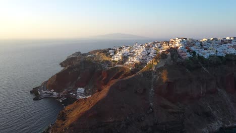 Drone-video-of-famous-whitewashed-and-colourful-picturesque-village-of-Oia-built-on-a-cliff-during-sunset,-Santorini-island,-Cyclades,-Greece