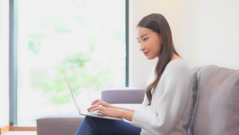 Side-view-woman-working-on-laptop-computer-smiling-at-home-interior