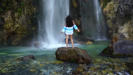 Girl-enjoying-freshness-of-waterfall-droplets-standing-on-cliff,-beautiful-spot-in-Theth,-Albania