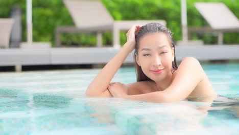 Portrait-of-Smiling-happy-Asian-female-in-a-bikini-inside-swimming-pool-looking-aside-and-into-the-camera