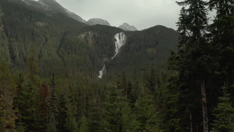 Drone-reveal-of-huge-waterfall-between-mountain-valley-in-pine-tree-forest