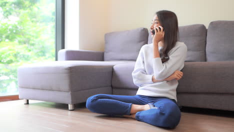 Woman-talking-on-phone,-Smiling-Asian-Thai-girl-sitting-on-floor-next-to-sofa-in-casual-clothes-and-having-a-flirting-mobile-phone-conversation