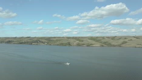 Small-boat-sailing-on-huge-lake,-green-hill-in-background