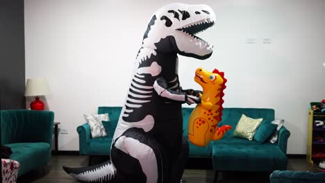 Halloween-Dinosaurierkostüm-Mit-Mann-Im-Wohnzimmer-Des-Hauses-Mit-Einem-Kleinen-Dinosaurier