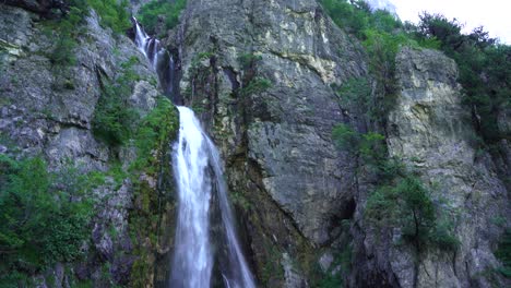 Vista-Ascendente-De-La-Hermosa-Cascada,-Agua-Fría-Y-Limpia-Que-Cae-De-Las-Montañas-Rocosas-En-Theth,-Albania