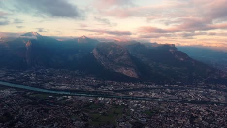Aerial-panoramic-footage-of-Grenoble-city-between-the-river-and-high-alps-mountain-during-amazing-cloudy-sunset