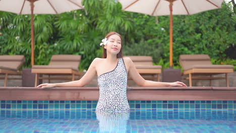 A-young-woman-stands-in-the-shallow-end-of-a-resort-swimming-pool-leans-along-the-edge-of-the-pool