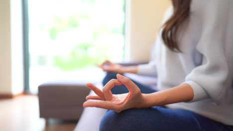Close-up-hands-of-pretty-fit-woman-practicing-yoga-sitting-on-sofa-in-lotus-position-meditating