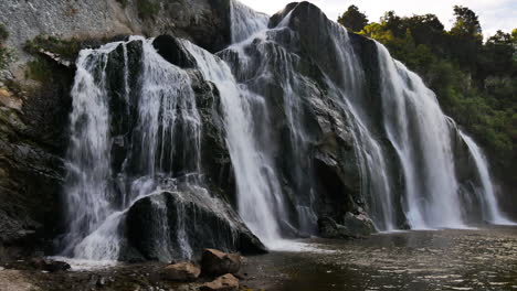 Panning-shot-of-gigantic-Waihi-Waterfall-flowing-into-idyllic-lake-in-New-Zealand,-Manawatu-Wanganui