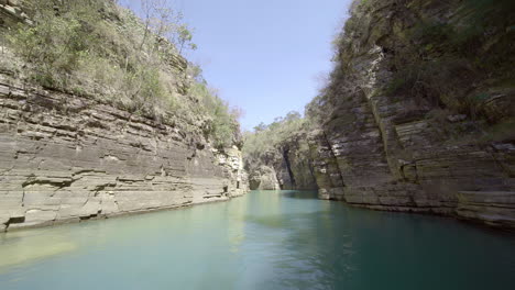 Boat-navigating-trough-canyons-of-sedimentary-rocks,-vegetation-and-green-water