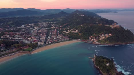 Aerial-view-of-San-Sebastián-city-in-Basque-Country-region-of-north-Spain,-lighthouse-in-the-middle-of-the-bay-and-stunning-sunset-view