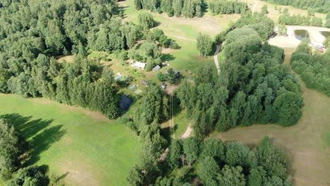 Beautiful-old-homestead-surrounded-by-forest-and-meadow,-aerial-descending-view
