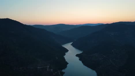 Aerial-view-of-an-amazing-river-path-during-sunset-over-some-pinewood-valleys