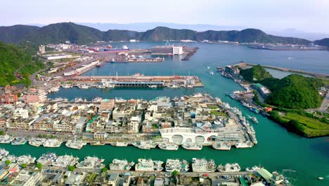 Aerial-view-of-Suao-Harbor-with-many-docking-boats-and-houses-on-island---Beautiful-mountain-scenery-in-background