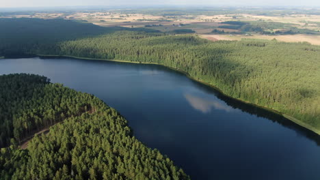 Blue-water-of-lake-Aviris-in-Lithuania-with-dense-forest-around,-aerial-high-angle-drone-view