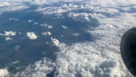 Top-down-shot-of-Airplane-Window-View-showing-flying-clouds-and-rural-valley-in-background