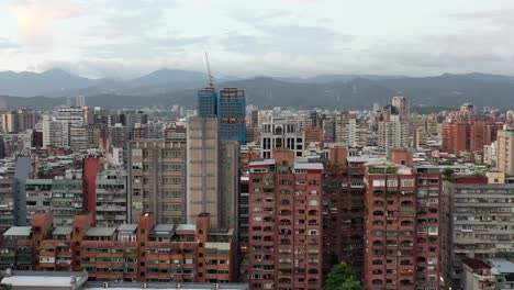 Aerial-tracking-shot-capturing-overly-crowded-high-density-population-living-in-Taipei-city,-rows-of-old-ageing-high-rise-apartments-facade-in-downtown-Xinyi-district,-with-mountainous-background
