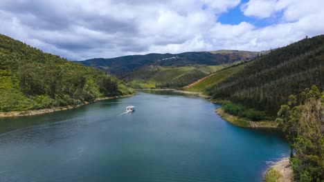Aerial-Hyperlapse-of-a-boat-sailing-through-a-river-surrounded-by-pinewood-forest-valleys-on-a-cloudy-sunny-day