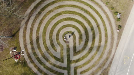 Person-standing-in-center-of-maze-and-walking-out-in-Birstonas,-aerial-ascend-top-down-view