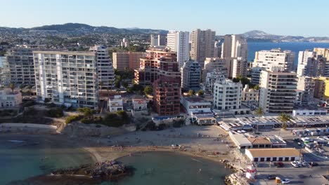 Drone-clip-over-a-beautiful-tropical-beach-in-Calpe,-Spain-with-hotels-and-resosrts-in-the-background