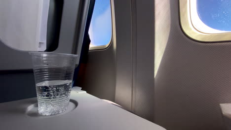 Airplane-Tray-Table-On-Seatback-With-Clear-Fresh-Bubbly-Sparkling-Water-In-Disposable-Cup