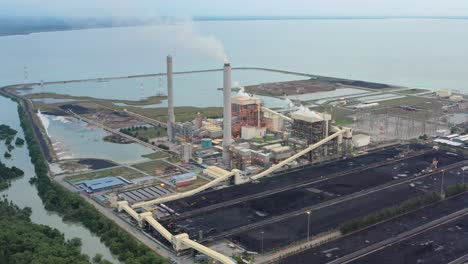 High-angle-pull-out-shot-capturing-large-coalfield-and-industrial-ultra-supercritical-coal-fired-power-plant-with-smokes-raising-from-chimney-located-at-costal-area-of-Manjung,-Perak,-Malaysia