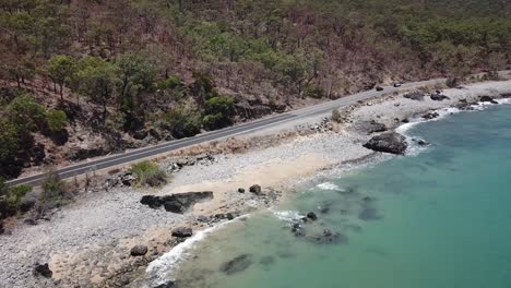 Drone-aerial-following-cars-and-pan-up-to-reveal-blue-tropical-water