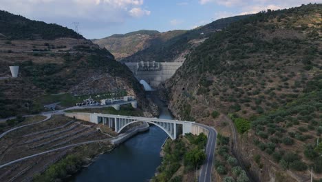 Aerial-view-of-a-bridge-and-a-river-dam-with-flowing-water-surrounded-by-mountains-and-valleys-on-a-sunny-day