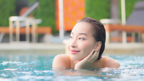 Charmante-Asiatische-Frau,-Die-Sich-Im-Pool-Entspannt-Und-Gesicht-Mit-Der-Hand-Hält