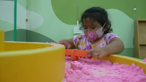 Asiatisches-Kleines-Mädchen,-Das-Mit-Plastikformen-spielzeug-Im-Sandkasten-Auf-Dem-Spielplatz-Im-Einkaufszentrum-Spielt