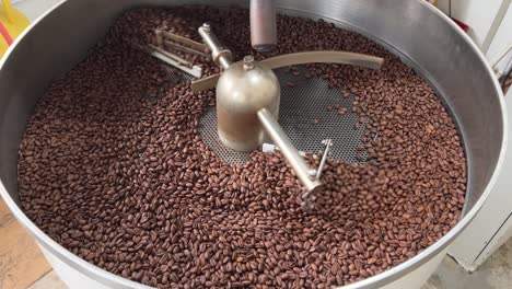 Fresh-specialty-coffee-beans-resting-on-cooling-and-mixing-tray-to-reduce-the-heat-evenly-after-roasting,-spinning-in-regular-speed,-production-warehouse-factory-shot-of-food-and-beverage-industry