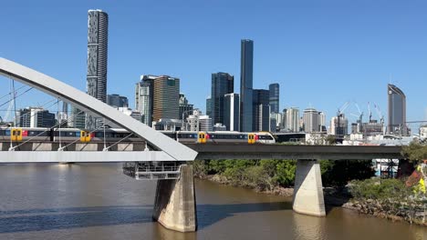 Railway-train-crossing-river-through-merivale-bridge-at-brisbane-city-from-northern-side-to-southern-side-with-downtown-cityscape-background,-translink-queensland-rail,-qld,-australia