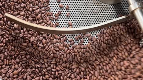 Quality-coffee-beans-spinning-on-cooling-and-mixing-tray-to-reduce-the-heat-temperature-after-roasting,-production-warehouse-factory-shot-of-food-and-beverage-industry,-extreme-close-up-shot