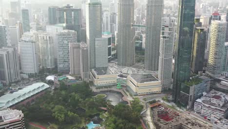 Tilt-up-shot-from-urban-greenery-klcc-park,-reveals-iconic-landmark-petronas-twin-towers-and-surrounding-downtown-cityscape-at-kuala-lumpur,-malaysia