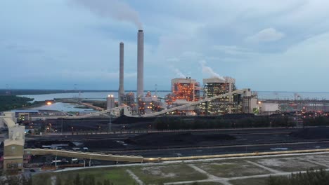 Fly-around-the-parameter-of-the-coalfield-and-industrial-ultra-supercritical-coal-fired-power-plant-with-smokes-raising-from-chimney-located-at-costal-area-of-Manjung,-Perak,-Malaysia-at-dusk