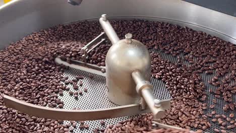 Specialty-coffee-beans-spinning-on-cooling-and-mixing-tray-to-reduce-the-heat-evenly-after-roasting,-production-warehouse-factory-shot-of-food-and-beverage-industry,-extreme-close-up-shot