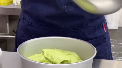 Scarping-off-matcha-cake-mixture-using-spatula-from-the-mixing-bowl-into-baking-mould,-delicious-soft-and-tasty-cake-making-in-progress,-close-up-shot