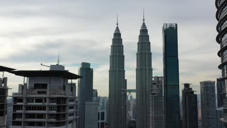 Reverse-shot-drone-flying-in-between-high-rise-skyscrapers,-capturing-spectacular-petronas-twin-towers-in-downtown-kuala-lumpur,-malaysia