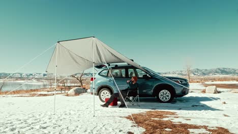 A-millennial-male-overlooks-a-gorgeous-winter-lake-underneath-a-camping-awning