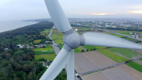 Close-up-shot-of-onshore-Wind-Turbine-rotating-in-front-of-plantation-fields-and-coastline-in-China---Aerial-backwards-flight