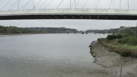 Low-aerial-flies-under-cable-bridge-on-muddy-River-Suir-in-Ireland