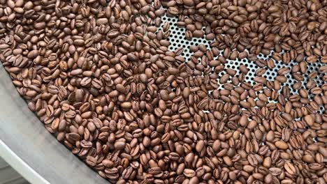 Quality-coffee-beans-spinning-on-cooling-and-mixing-tray-to-reduce-the-heat-temperature-after-roasting,-production-warehouse-factory-shot-of-food-and-beverage-industry,-close-up-shot