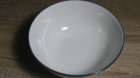 Weiße-Keramikschale-Auf-Dem-Tisch-Gezoomt,-Bevor-Sie-Beim-Frühstück-Mit-Müsli-Oder-Müsli-Gefüllt-Wird