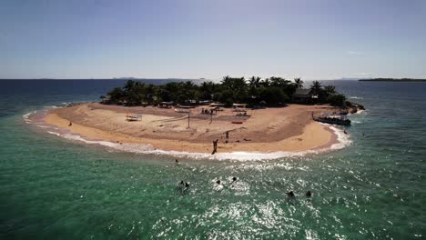 Drone-Estático-Con-Vistas-A-Una-Pequeña-Isla-Tropical-En-Fiji-Mientras-La-Gente-Nada-En-El-Agua-En-Un-Día-Azul-Claro