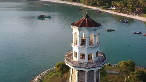 Cinematic-orbiting-shot-drone-fly-around-tourist-landmark-perdana-quay-light-house-with-fishing-boats-moored-on-the-gulf,-beautiful-scenery-at-langkawi-island,-kedah,-malaysia,-southeast-asia
