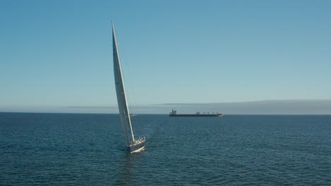 Wally-100ft-yacht-sailing-towards-camera,-Cargo-ship-in-distance,-Atlantic-Ocean